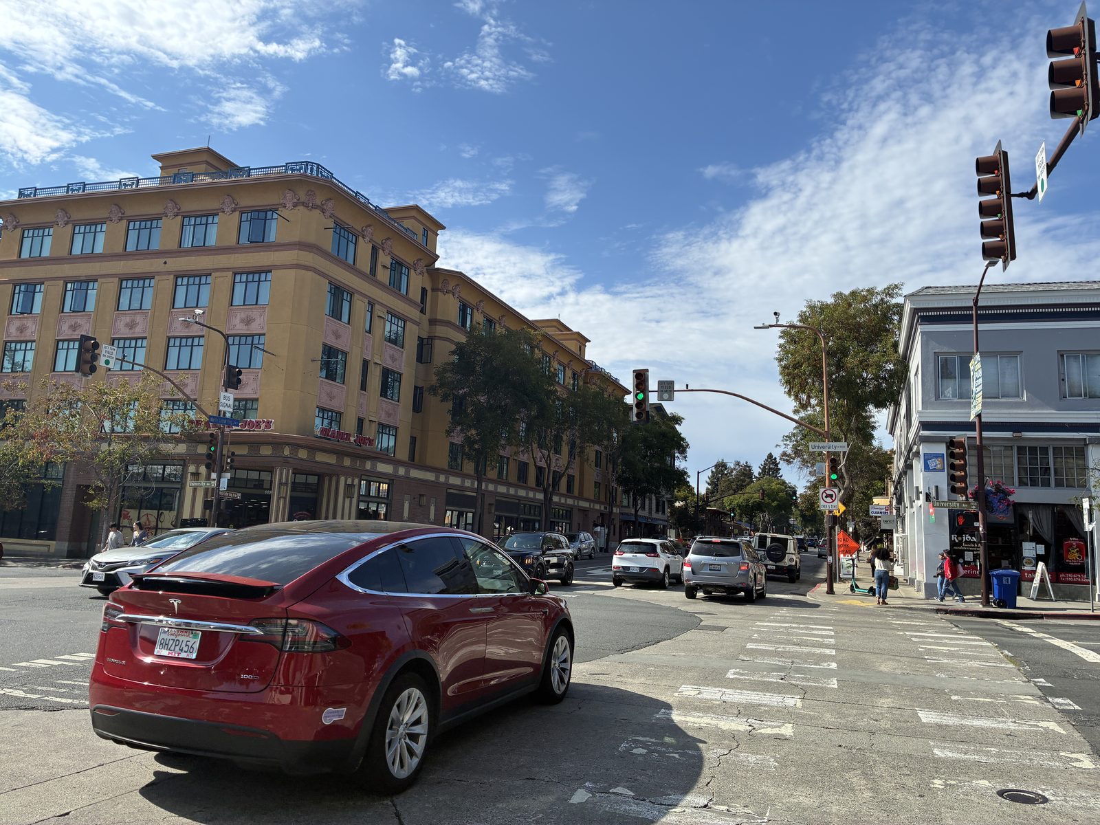 A big intersection on University Avenue, a red car waiting and a brick apartment block behind