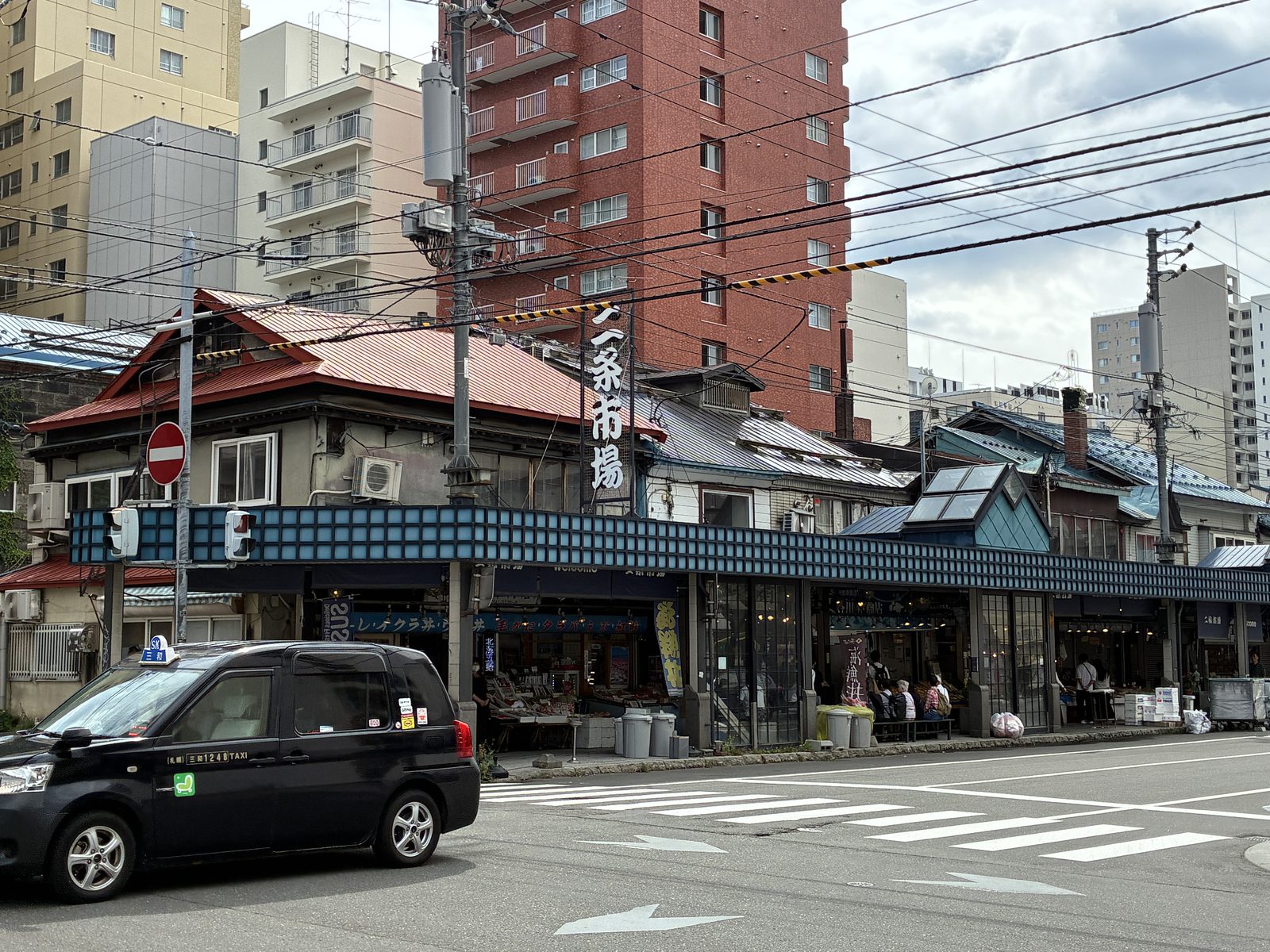 A crossing in central Sapporo, low older shopfronts under tall apartment blocks